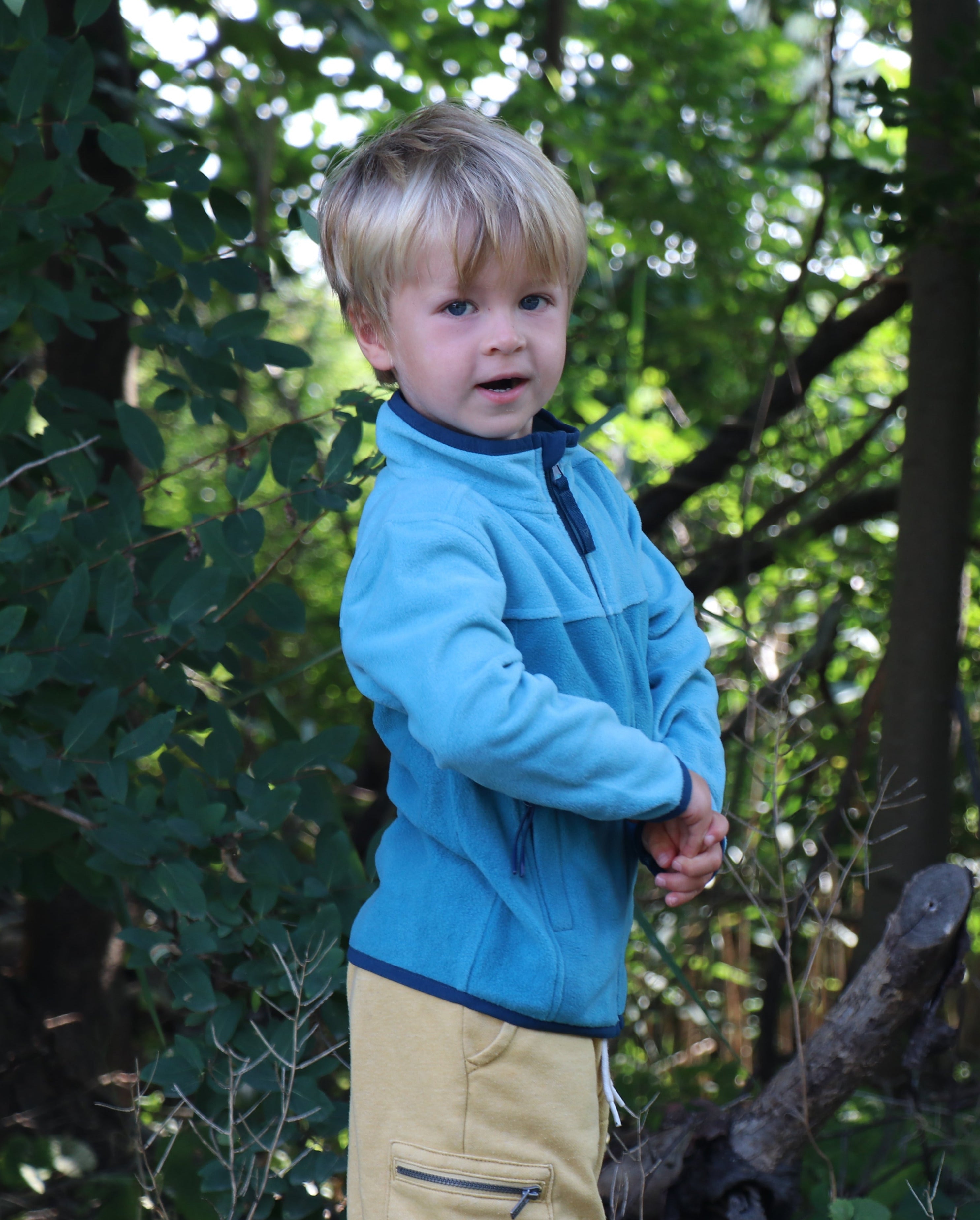 Child wearing a blue jacket standing in a forest